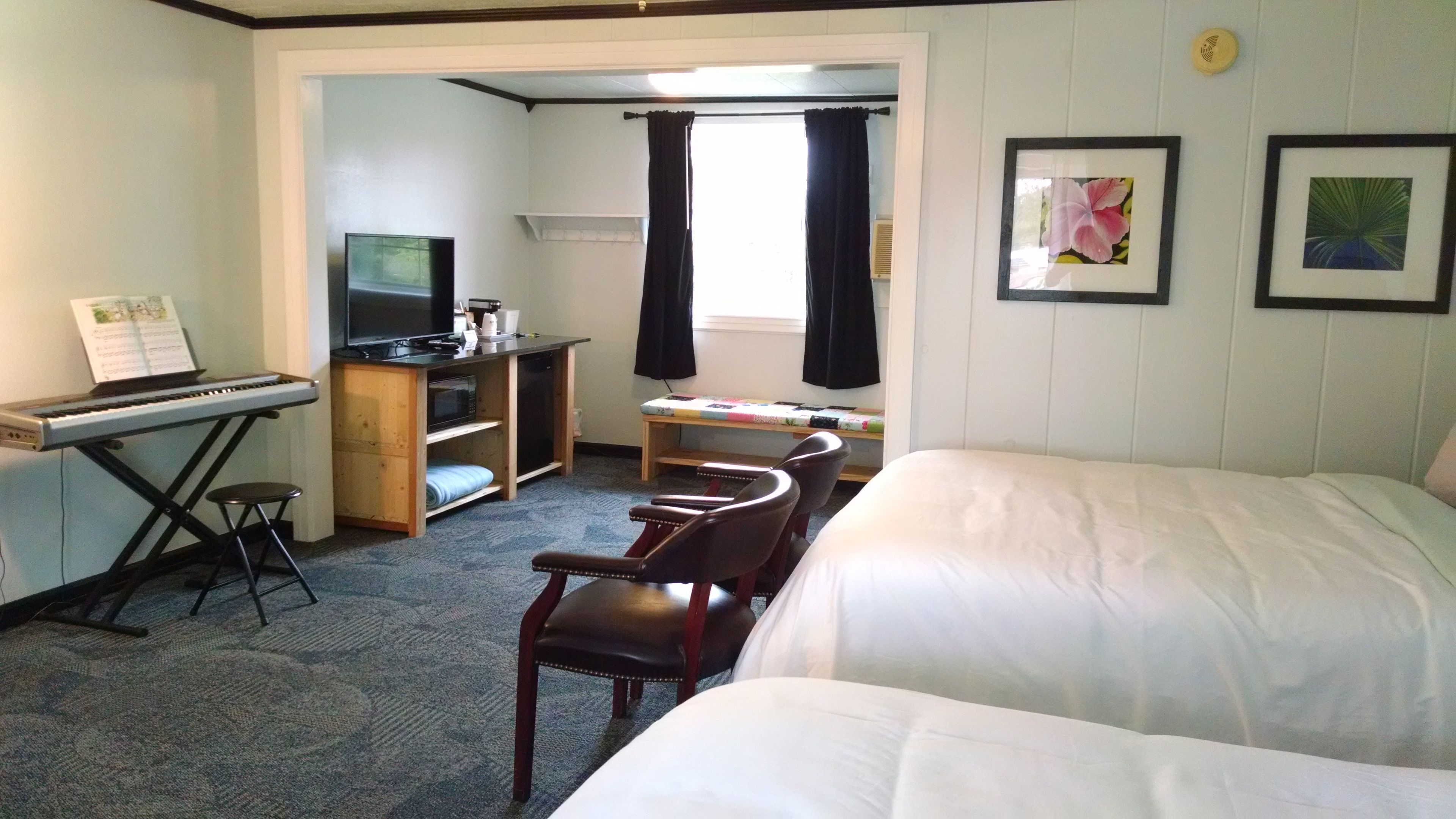 Une chambre d’hôtel avec un lit, un bureau doté d’un clavier et d’une télévision, une petite table avec une courtepointe, et deux tableaux encadrés accrochés au mur.