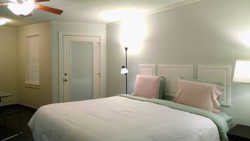A bedroom with a bed, a door, a floor lamp, and a window with blinds.