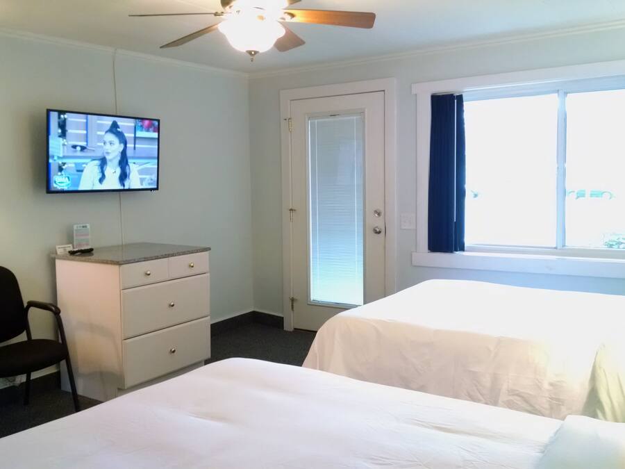A hotel room with a bed, a desk, a chair, a TV, and a window with curtains.