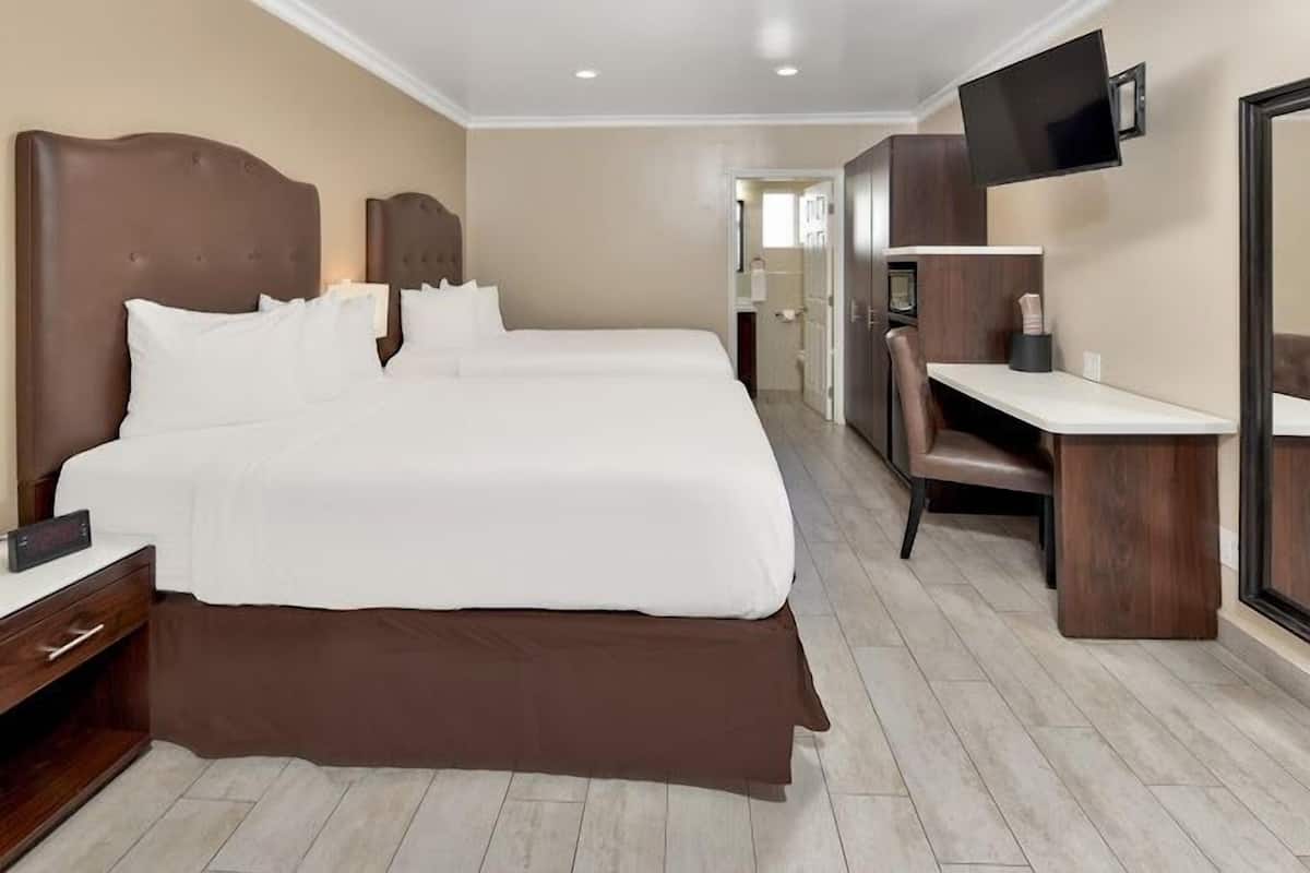 A hotel room with a double bed, a desk, a chair, a TV, and a bathroom visible through an open door.
