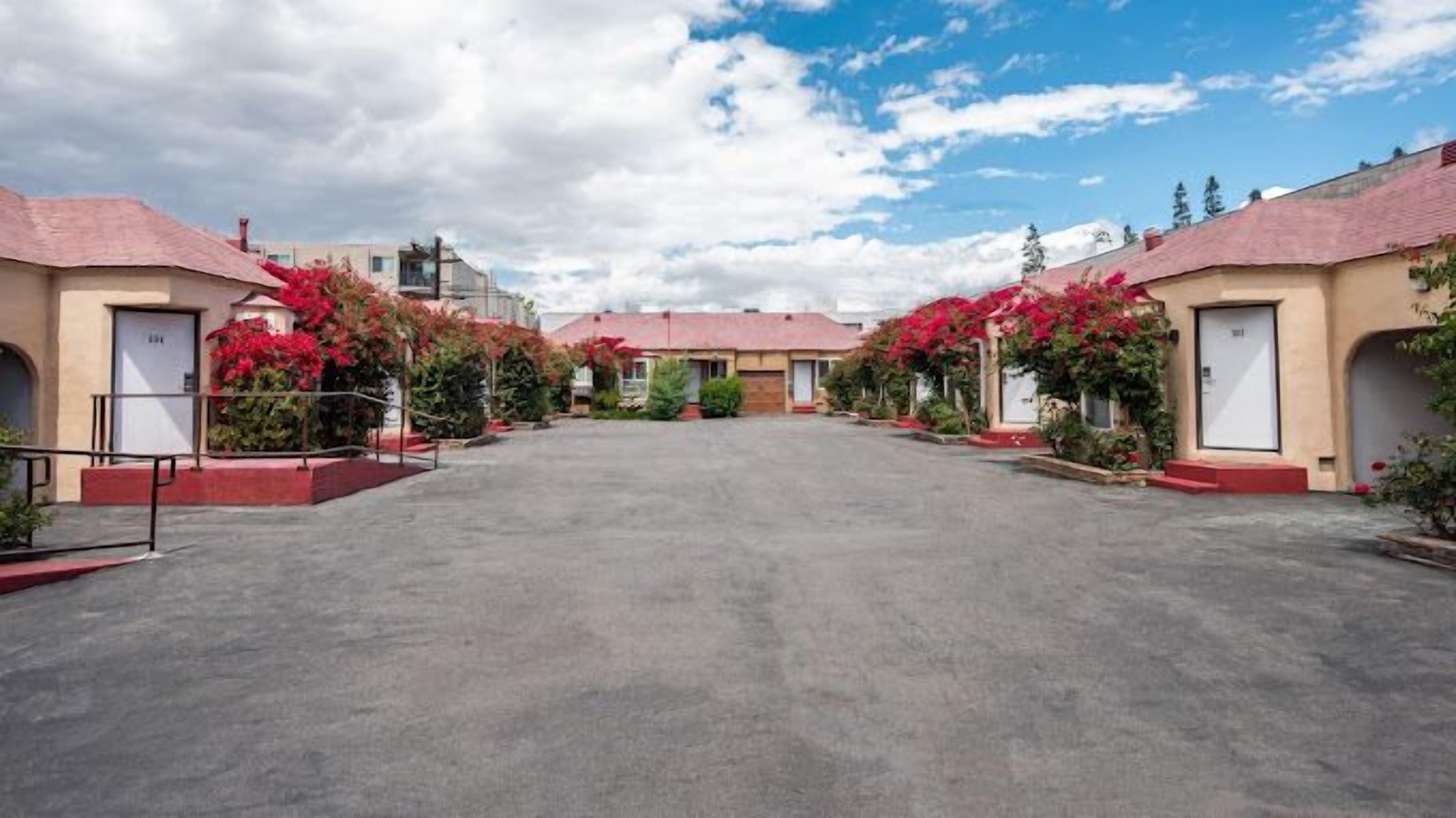 A row of motel buildings with red roofs and a central parking area.