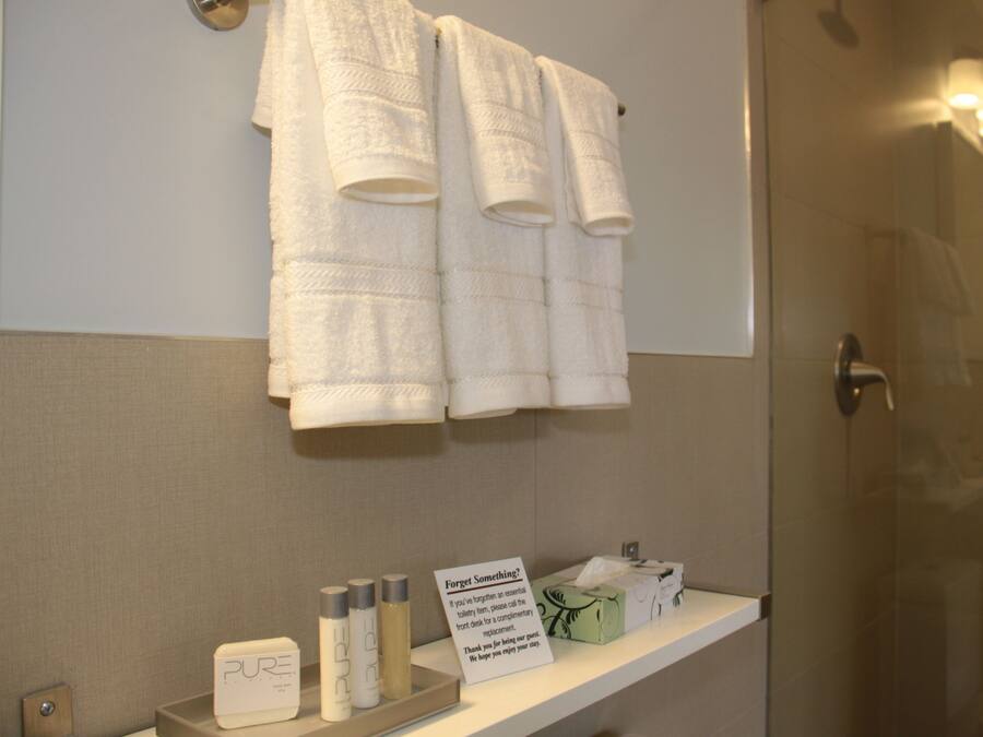 A bathroom with three white towels hanging on a wall, a shelf with toiletries, and a sign.