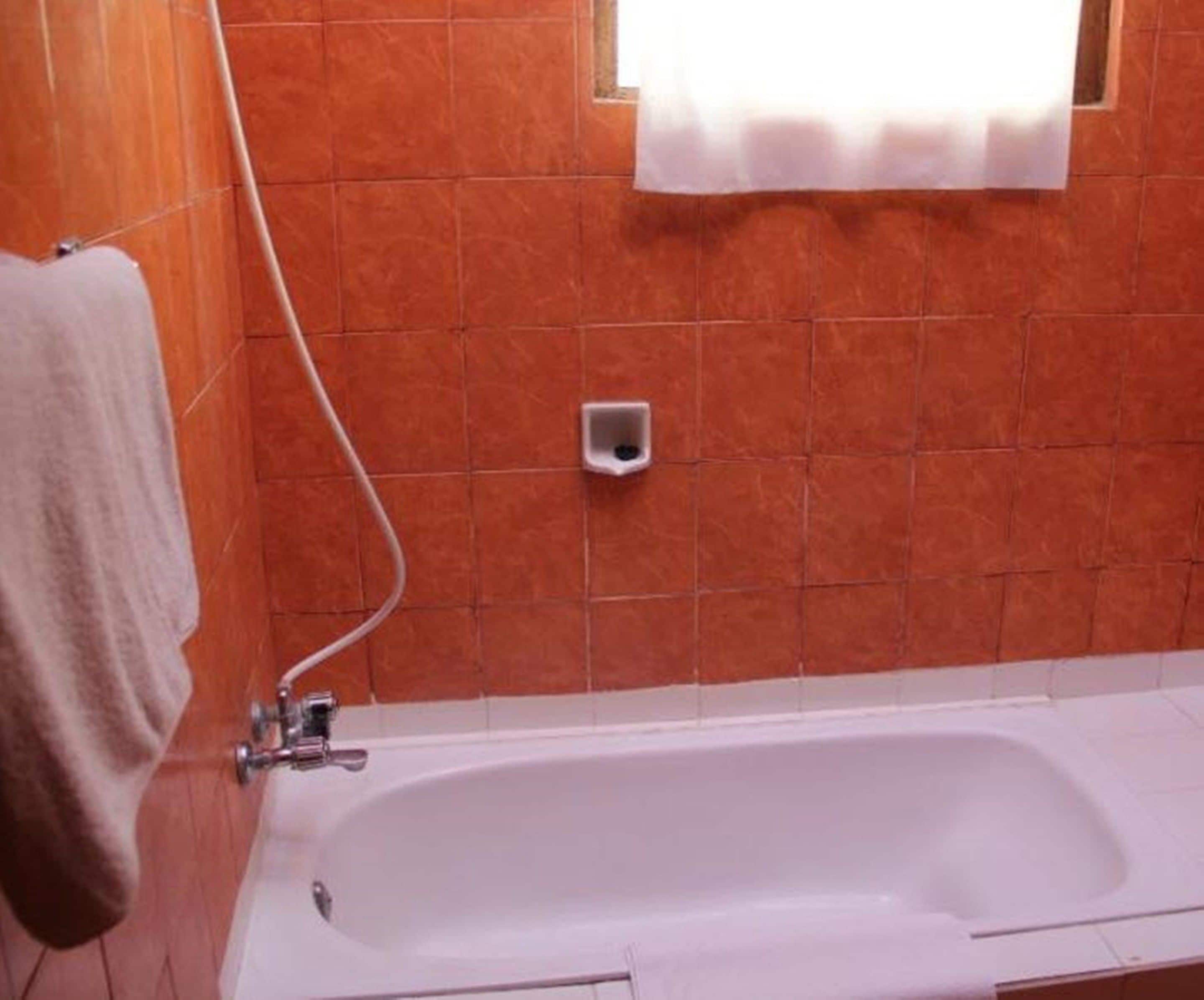 Une salle de bain avec une baignoire blanche, un porte-serviettes et une petite fenêtre avec un rideau.