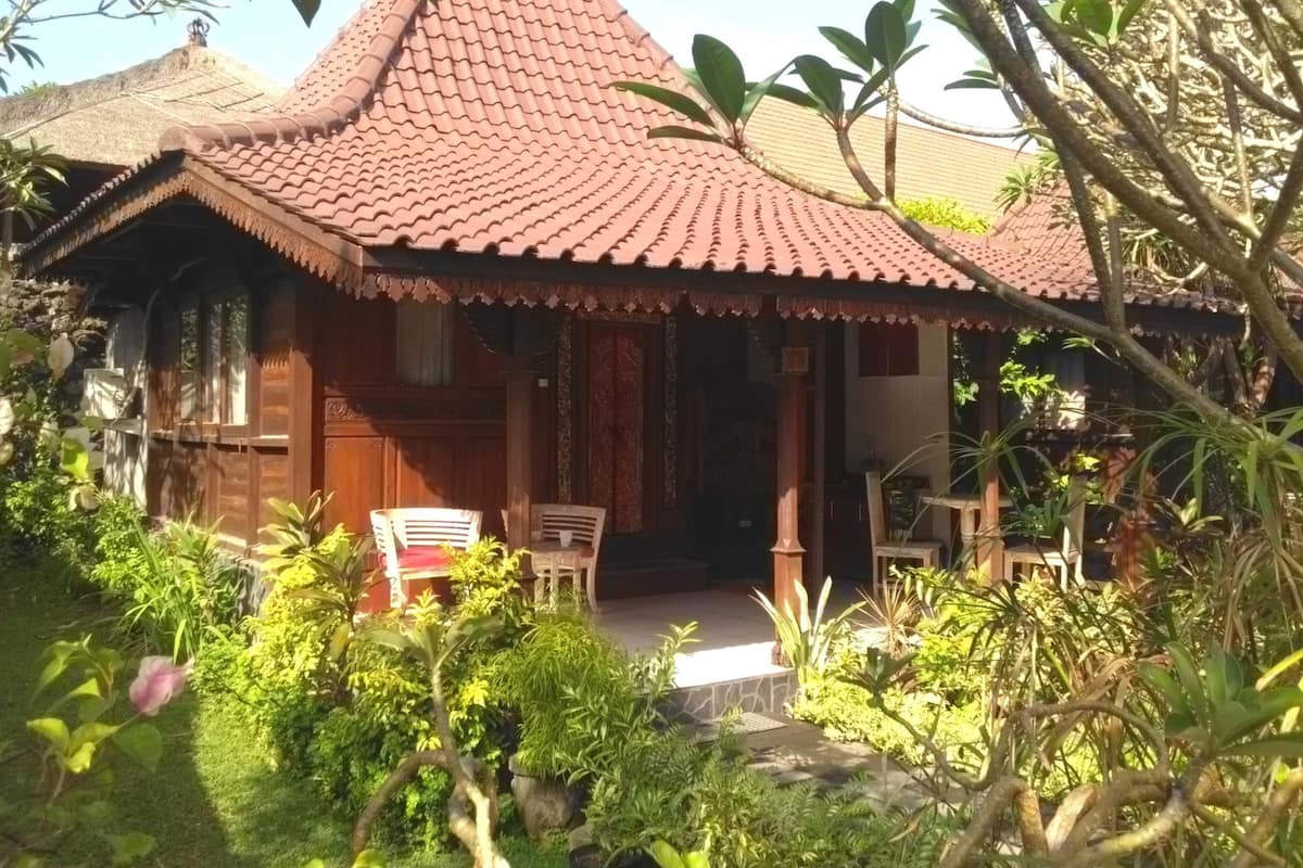 A traditional house with a tiled roof and wooden walls, surrounded by lush greenery and a small garden.