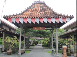 A traditional pavilion with a tiled roof, surrounded by potted plants and a pathway leading to a building with a sign reading "gatebo". - Gazebo Beach Hotel (Denpasar)