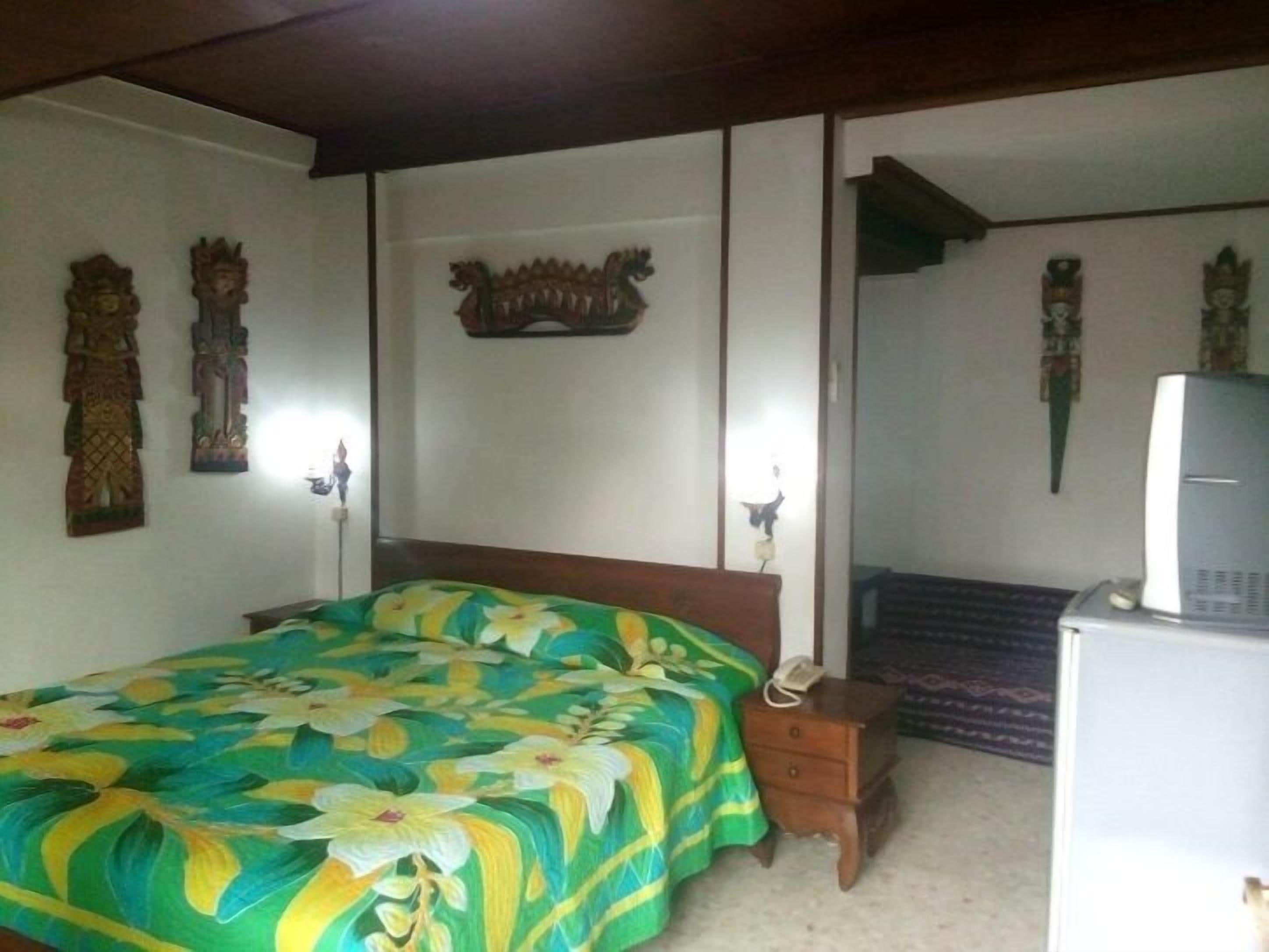 A bedroom with a bed, a nightstand, a desk with a computer, and decorative wall art.
