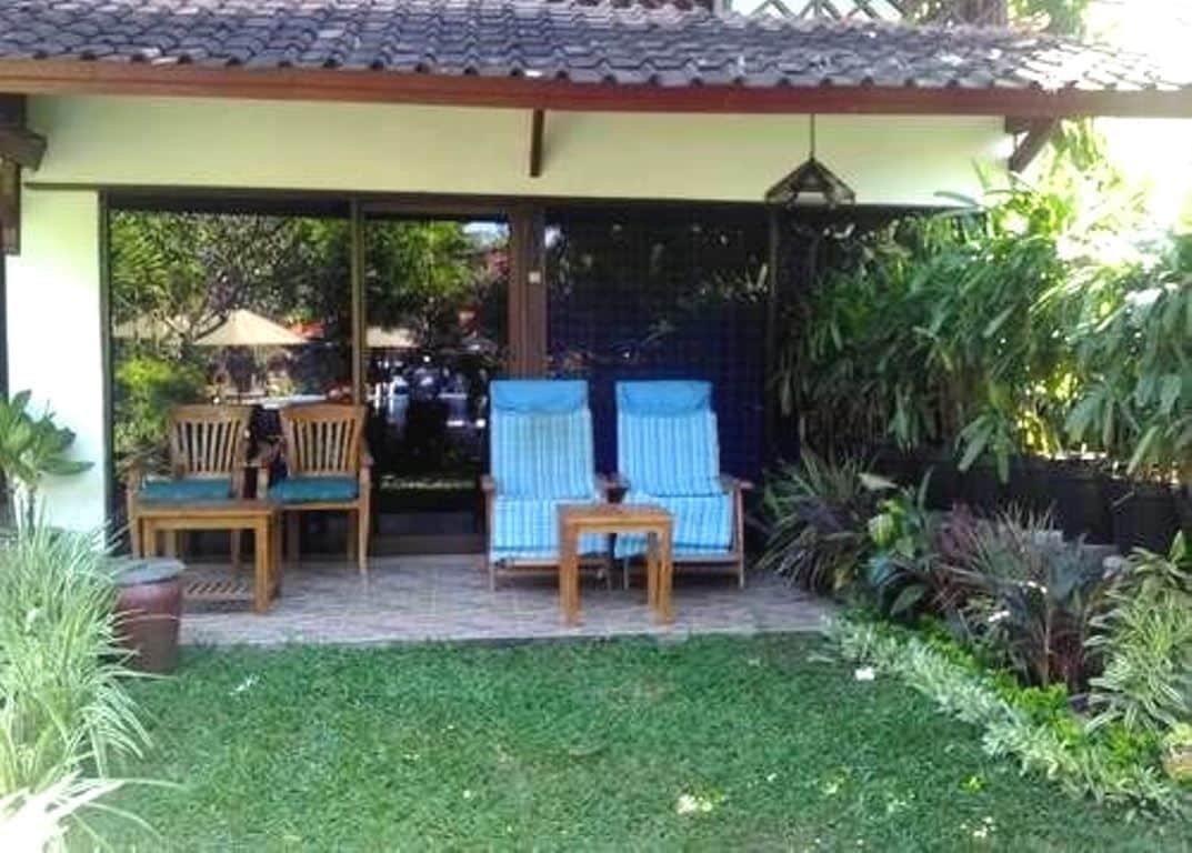 Un área de patio al aire libre con una zona de estar cubierta, una mesita y una lámpara colgante.