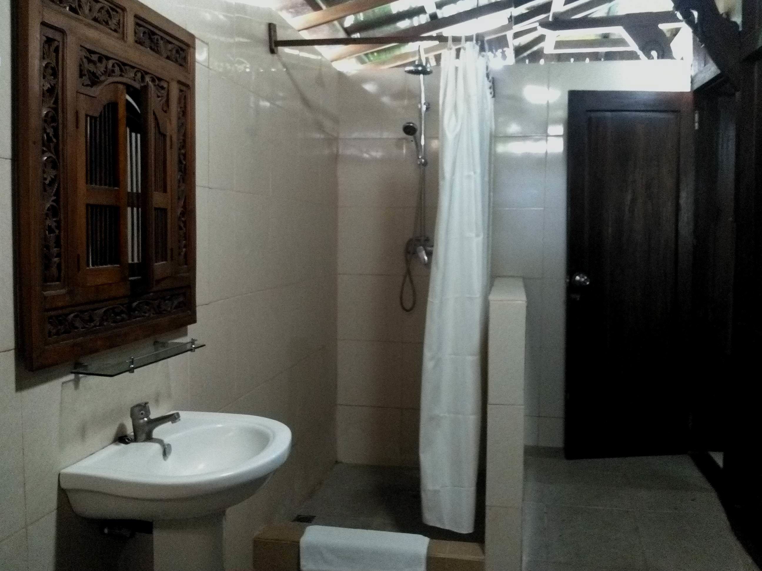 Un baño con lavamanos, ducha y un armario de madera sobre el espejo.