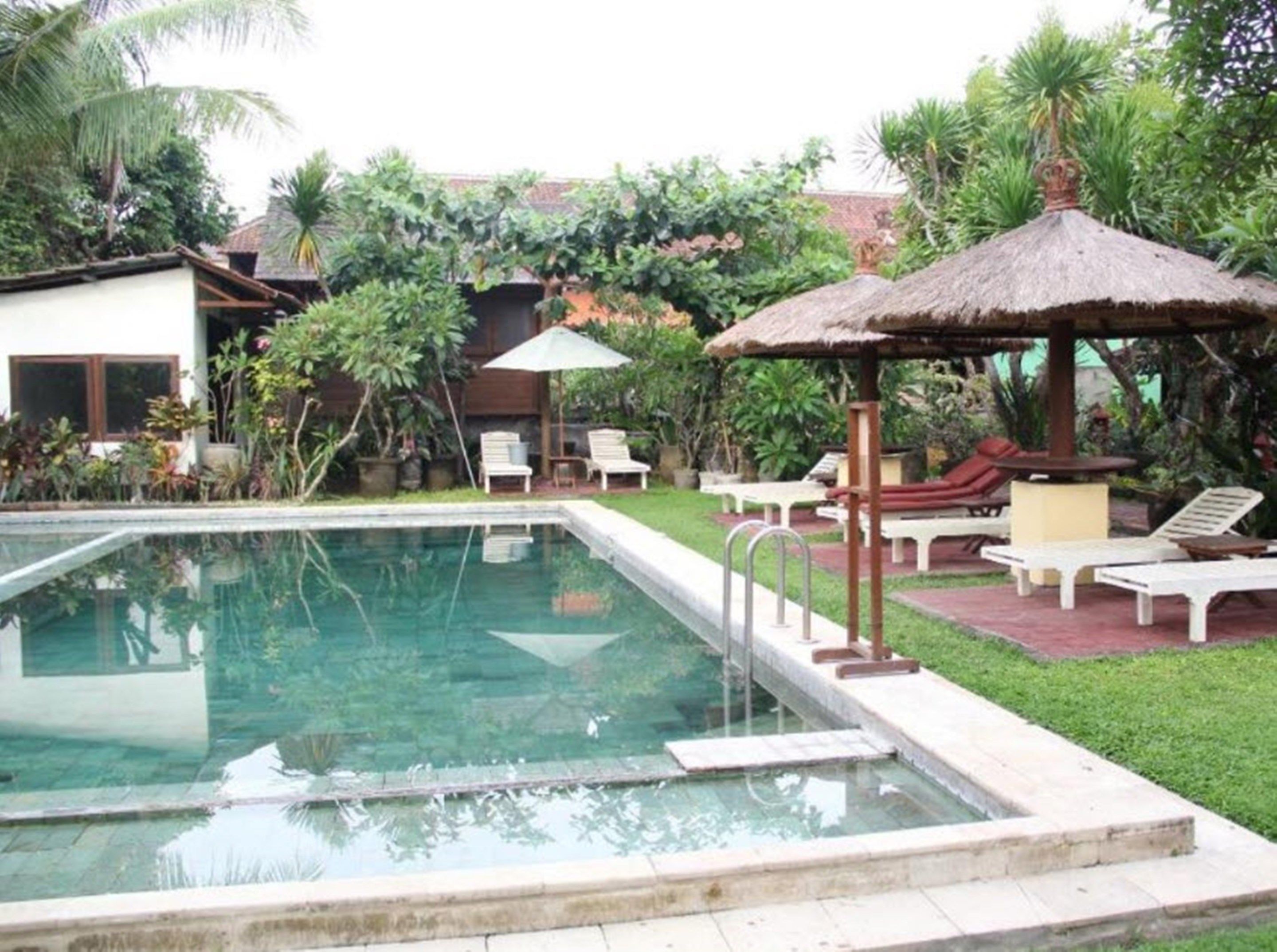 Ein Swimmingpool mit Liegestühlen und einer strohgedeckten Laube.