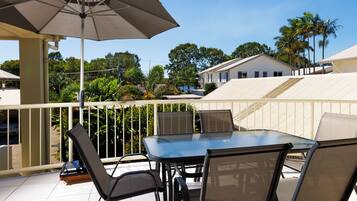 Een terras met een glazen tafel en stoelen, een parasol en uitzicht op huizen en bomen.