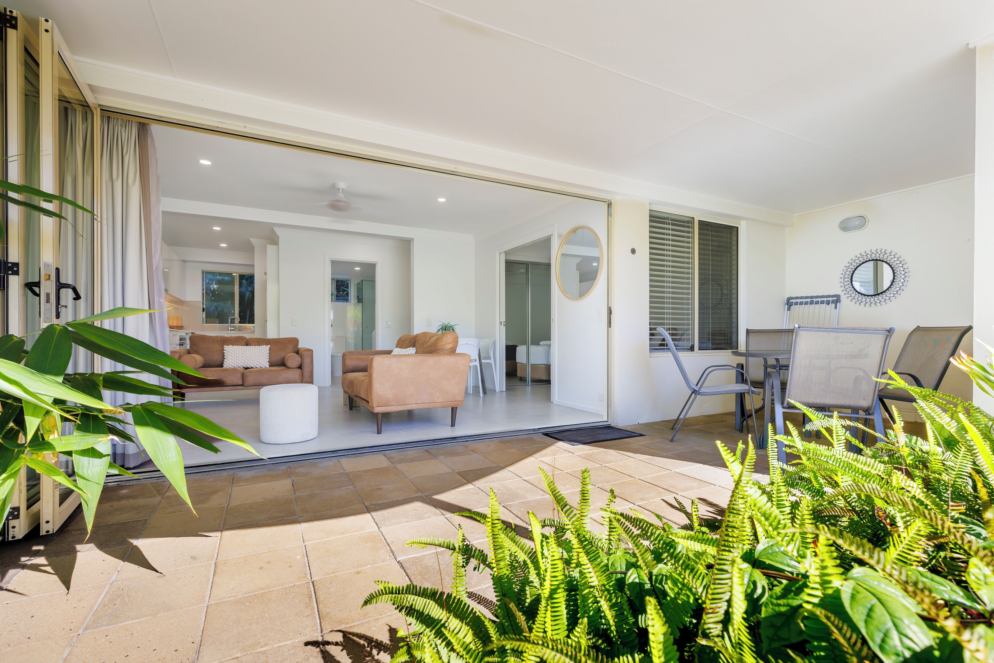 A spacious living area with a sliding glass door leading to a balcony, a sofa, a coffee table, and a dining area with chairs.
