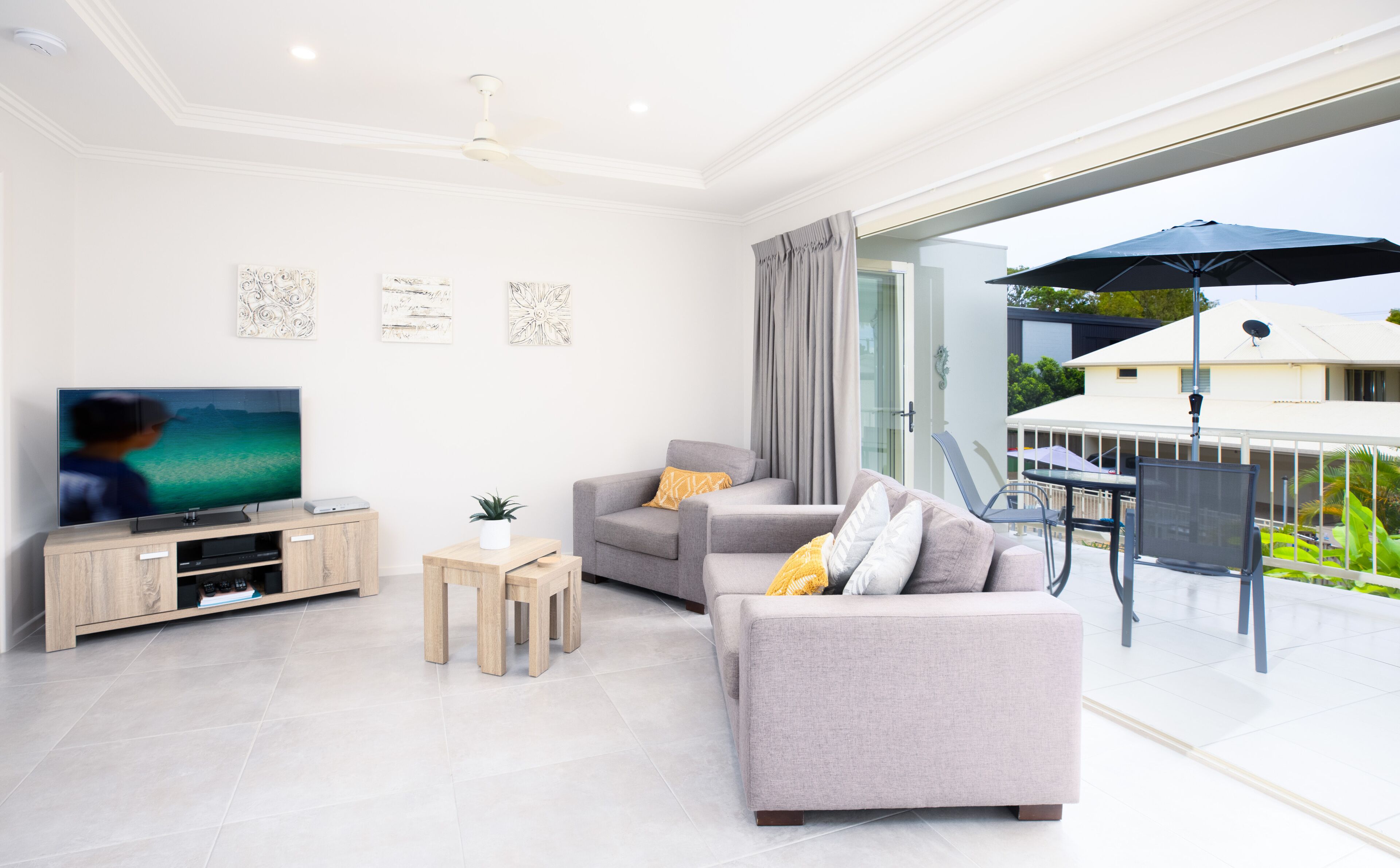 En moderne stue med et fladskærms-tv, grå sofaer, et sofabord og en balkon med et bord og parasol.
