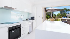 A modern kitchen with white cabinetry, a black oven, and a dishwasher. There is a large island with a bowl and a coffee machine.