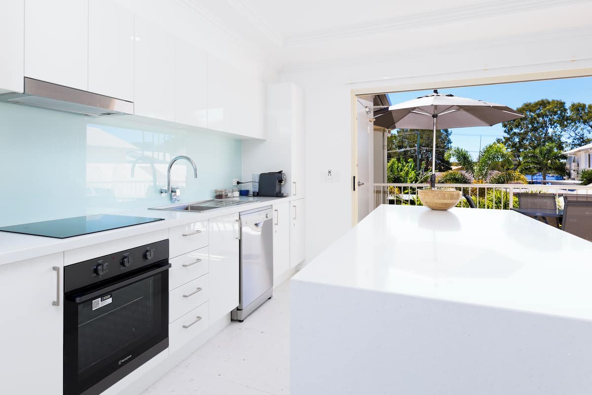 Una cucina moderna con mobili bianchi, un forno nero e una lavastoviglie. È presente una grande isola con una ciotola e una macchina da caffè.