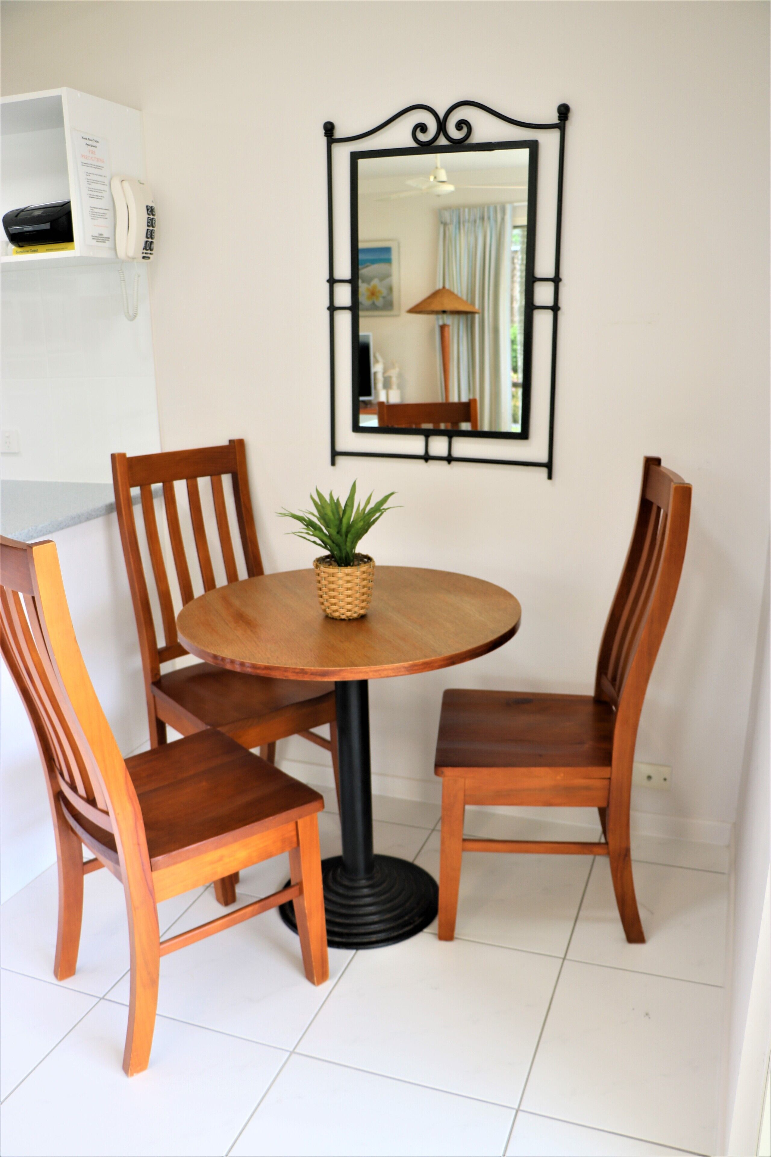 A dining area with a round wooden table, four wooden chairs, a potted plant, and a wall-mounted mirror.