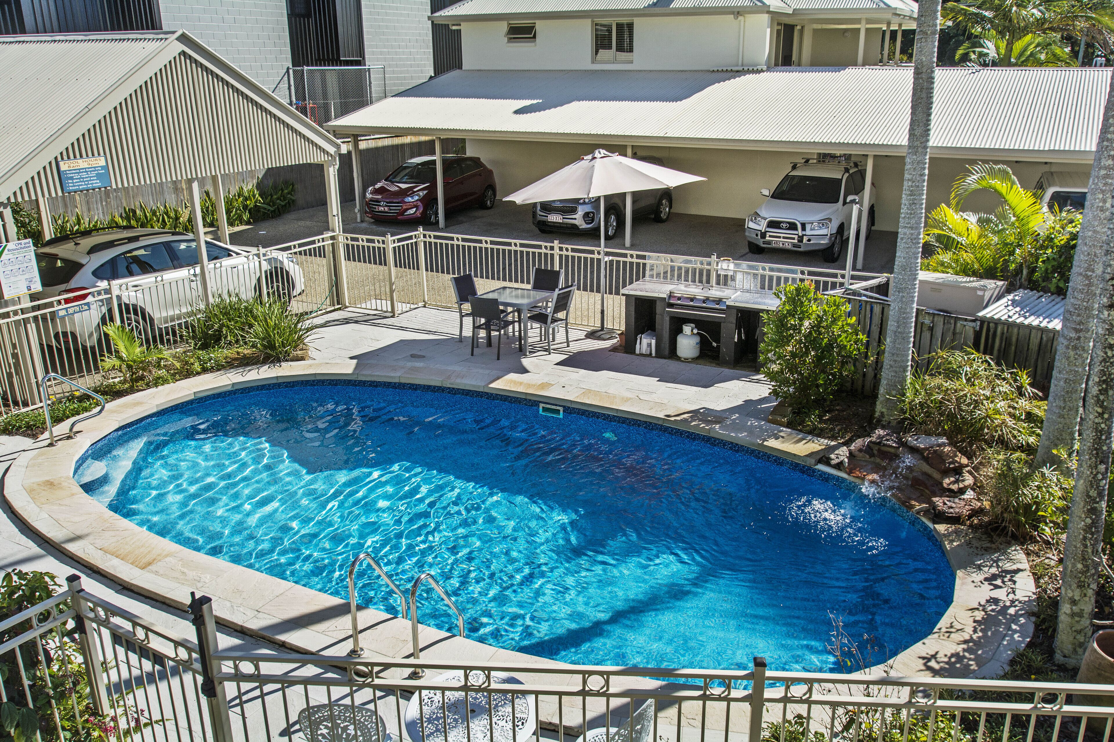 A swimming pool with a patio area, a covered carport, and a fenced yard.