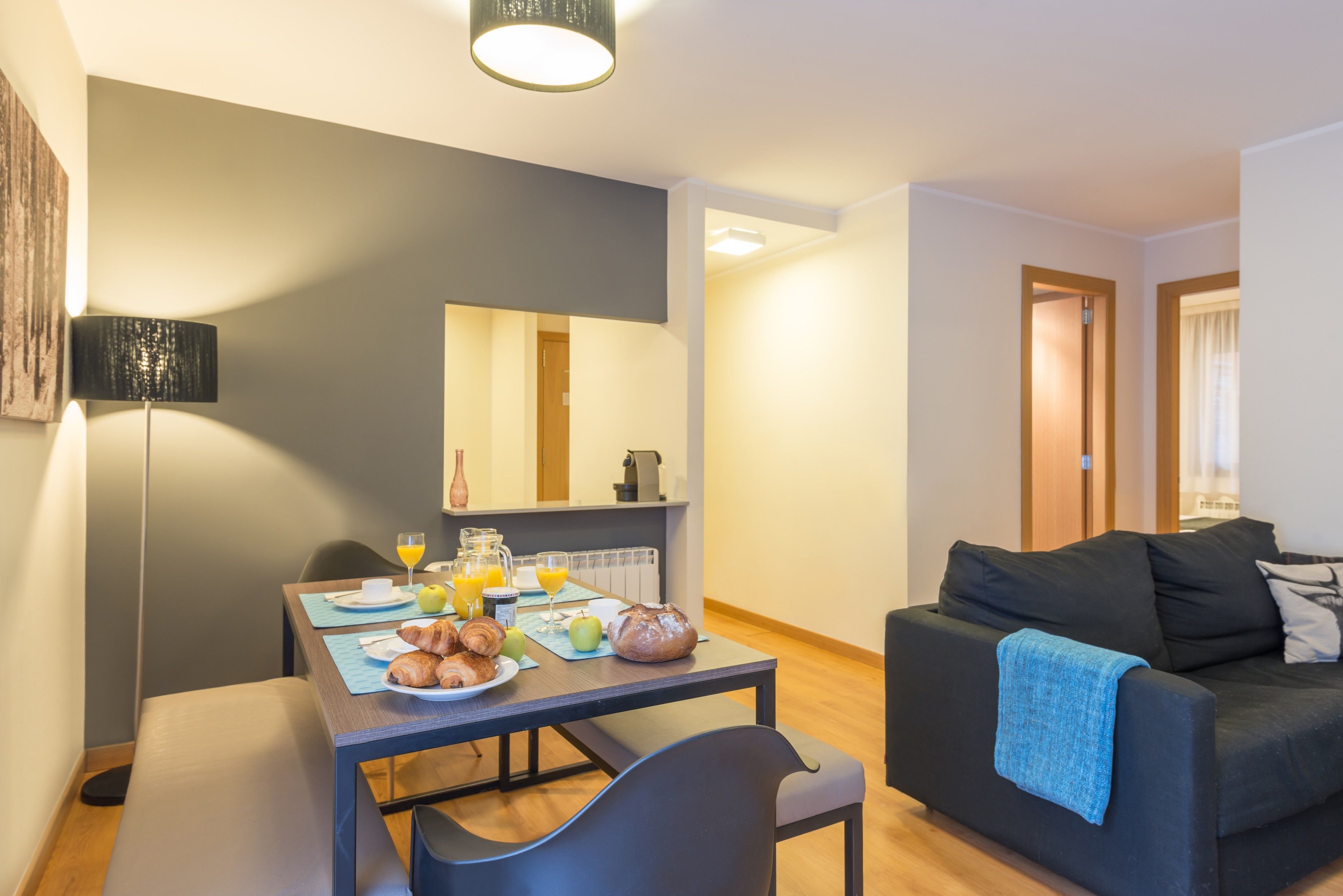 Una sala de estar moderna con comedor, que incluye un sofá, una mesa de desayuno y una lámpara.