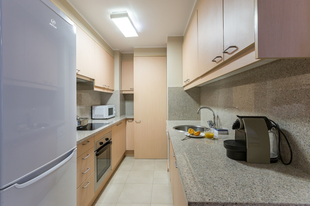 A compact kitchen with a refrigerator, microwave, oven, sink, and a coffee machine.