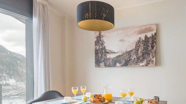 A dining area with a table set for breakfast, a bench, and a view of a snowy landscape through a window. - Pierre & Vacances Andorra El Tarter (El Tarter)
