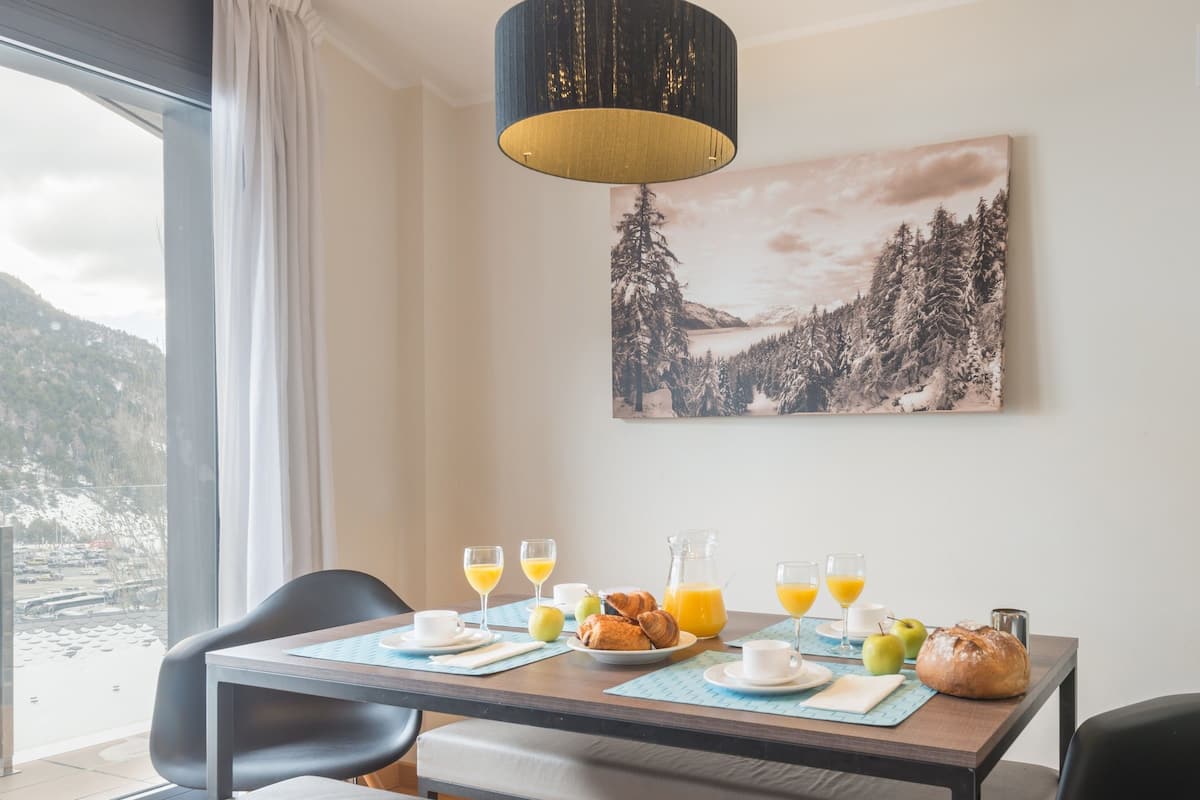 A dining area with a table set for breakfast, a bench, and a view of a snowy landscape through a window.