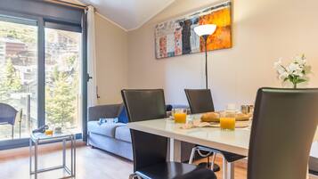 Un coin repas avec une table dressée pour deux personnes, des chaises, un vase rempli de fleurs et un tableau accroché au mur.