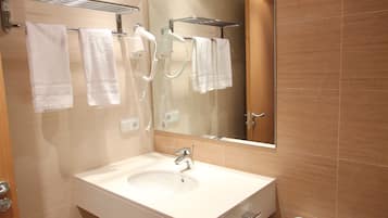 Un baño moderno con lavamanos, espejo y retrete blancos. Hay dos toalleros con toallas colgadas.