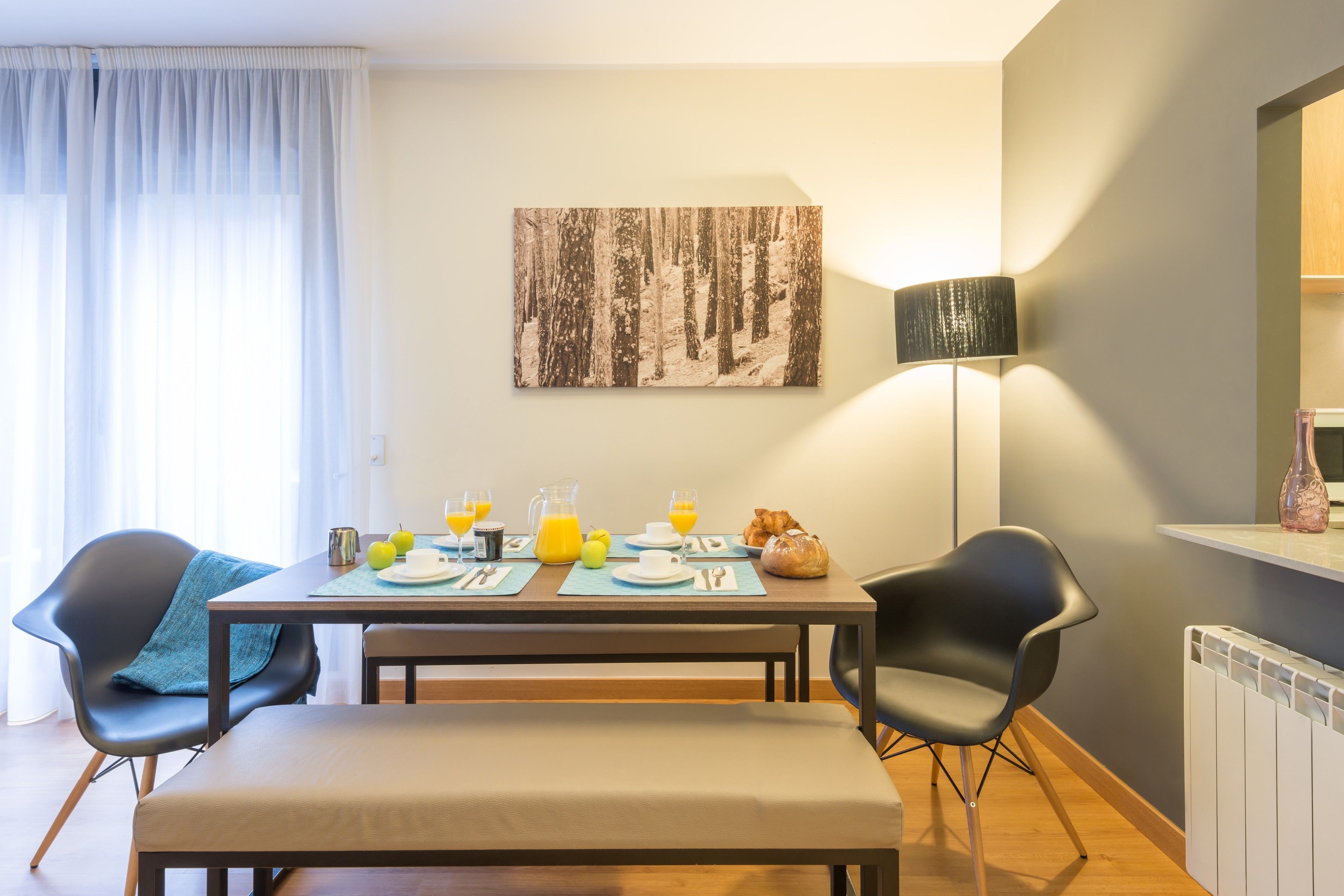 A dining area with a table set for two, a lamp, and a painting on the wall.