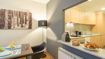 Una cocina moderna con armarios de madera, un comedor con una mesa lista para dos comensales, y un cuadro grande de un bosque en la pared.