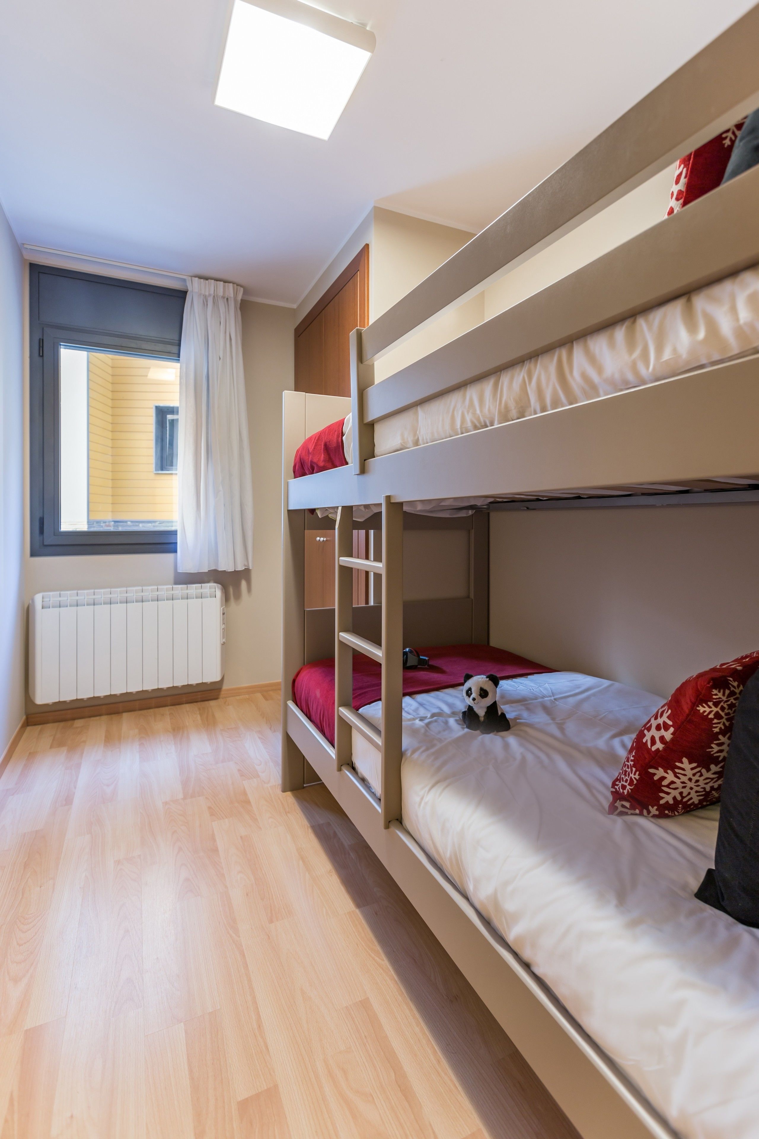 A bunk bed room with a window, radiator, and a panda plush toy.