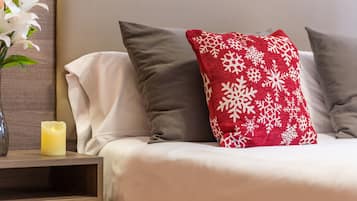 A neatly made bed with white and gray bedding, a red pillow with white snowflakes, and a lit candle on a bedside table.