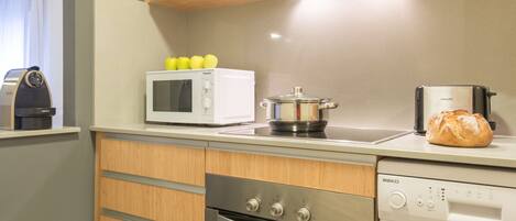 A compact kitchen with wooden cabinets, a microwave, a toaster, an oven, and a dishwasher.