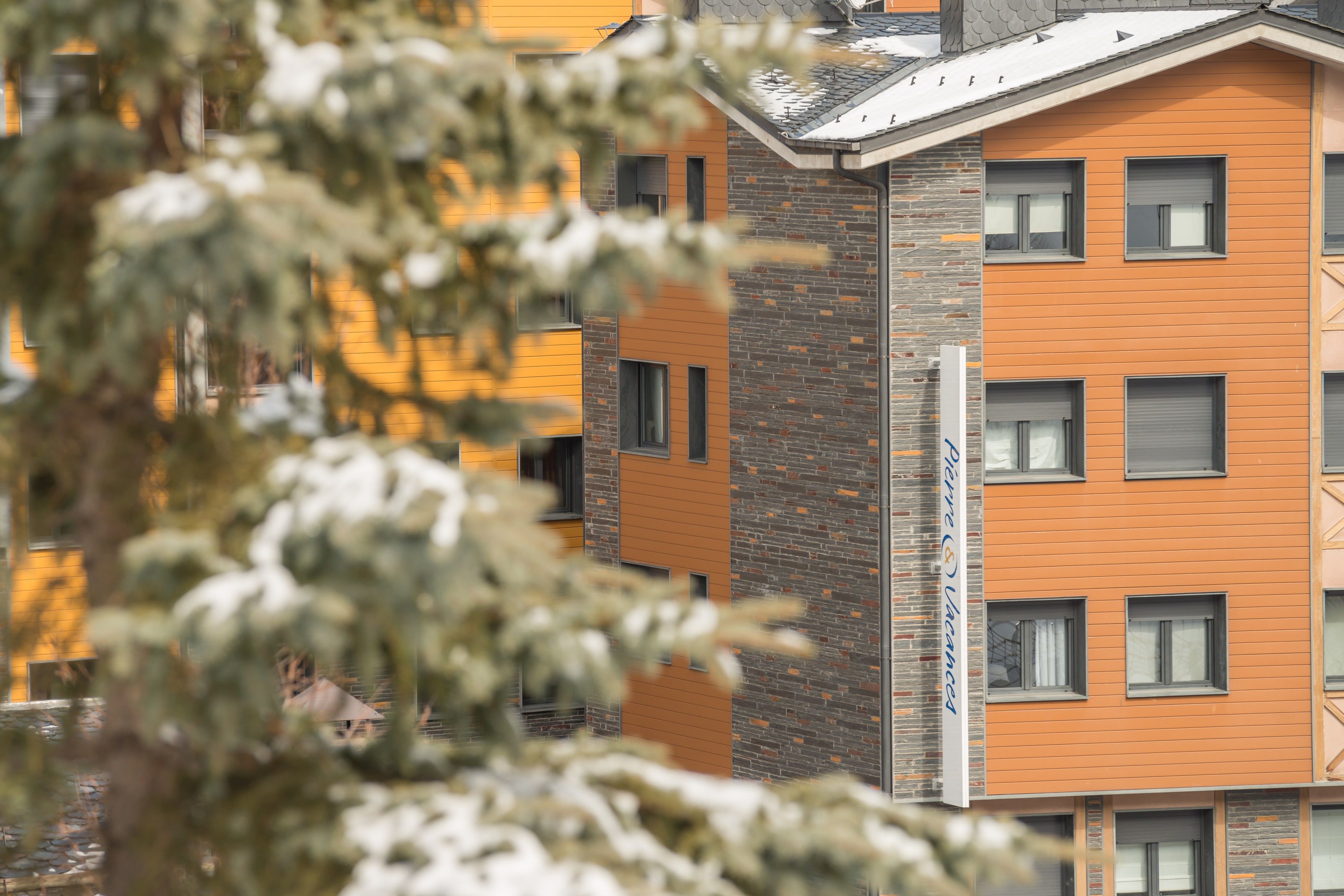 Un immeuble à plusieurs étages, doté d’une façade en briques et de panneaux orange, avec de nombreuses fenêtres et des balcons.