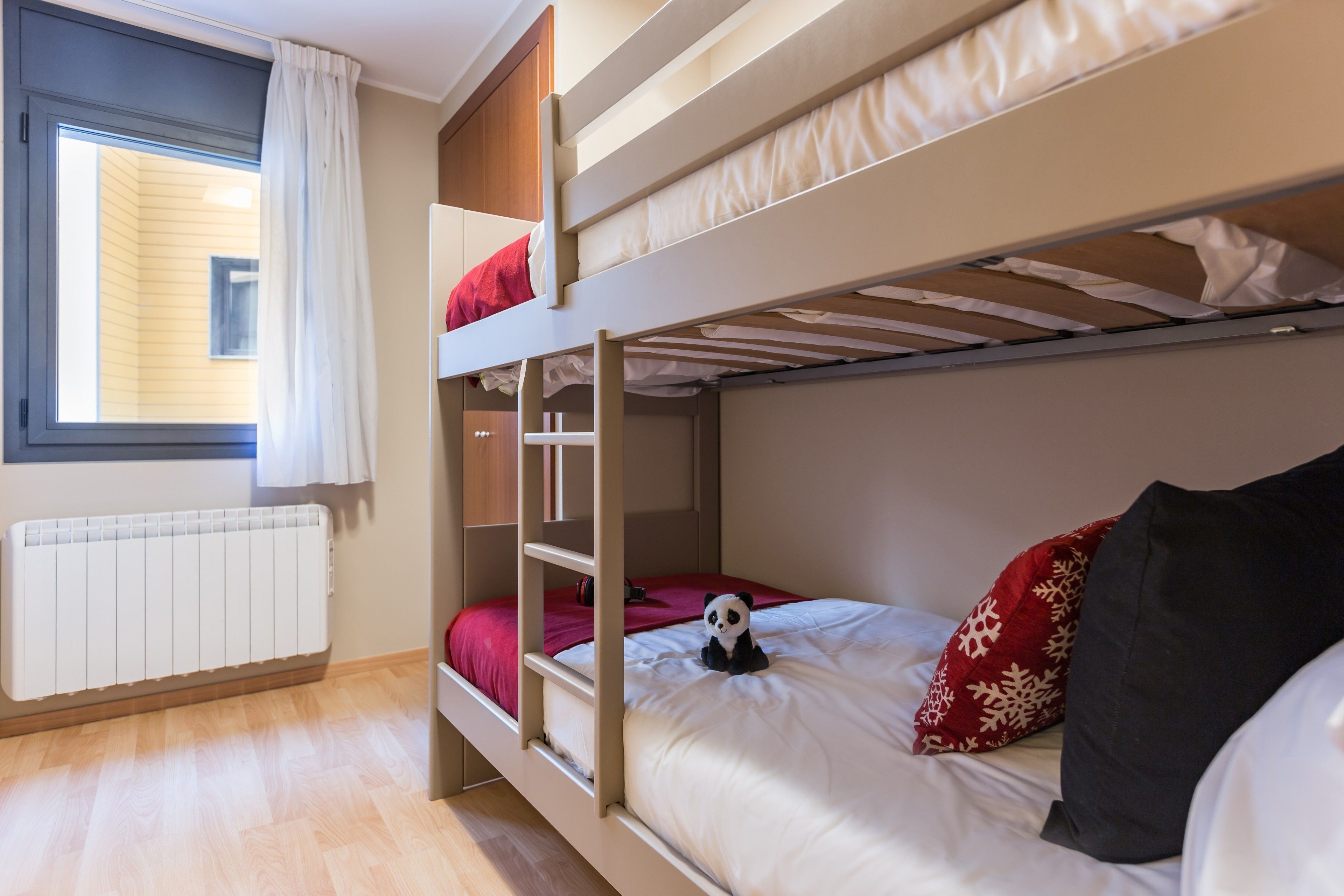 A bunk bed room with a window, a radiator, and a panda plush toy.