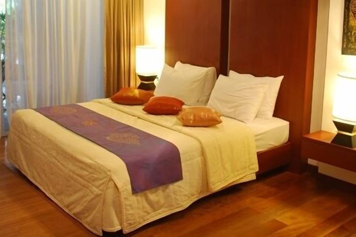 A hotel room with a bed, two bedside tables, a nightstand, a window with curtains, and a wall with artwork.