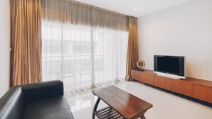 Una sala de estar moderna con un sofá, una mesa de centro de madera, un televisor de pantalla plana sobre un mueble de madera y cortinas translúcidas.