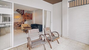 Amplio espacio interior con una escalera de madera que sube a un nivel superior, una zona de estar con sillas y un gran ventanal corredizo hacia el exterior.