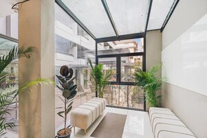 Un interior moderno con techo de vidrio, una zona de estar con sofá y reposapiés, y plantas en macetas.