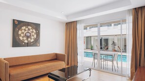 Una sala de estar moderna con sofá, una mesa de centro de vidrio y un ventanal con vistas a una piscina y zona de estar exterior.