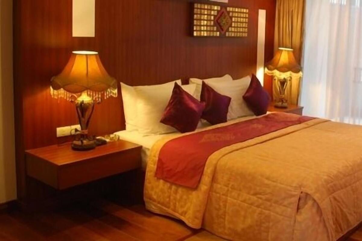 A neatly made bed with a red blanket, two bedside lamps, and a wooden headboard.