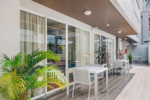 Un patio exterior moderno con puertas de cristal, mobiliario blanco y plantas en macetas.