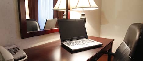 A hotel room with a wooden desk, a laptop, a telephone, and two lamps.