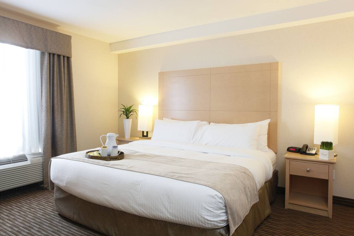 A hotel room with a large bed, bedside tables, a lamp, and a window with curtains.