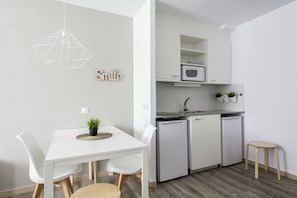 A modern kitchen with white cabinetry, a microwave, and a sink. There is a dining table with chairs and a small stool. - Residencia Universitaria Resa Manuel Agud Querol (San Sebastián)