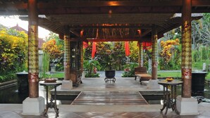 A covered outdoor area with a tiled floor, wooden pillars, and a central seating area with a table and chairs. - Bumi Ubud Resort (Ubud)