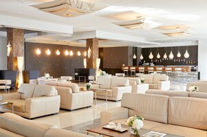 Un moderno vestíbulo de hotel con varias zonas de estar, un mostrador de recepción y un bar.
