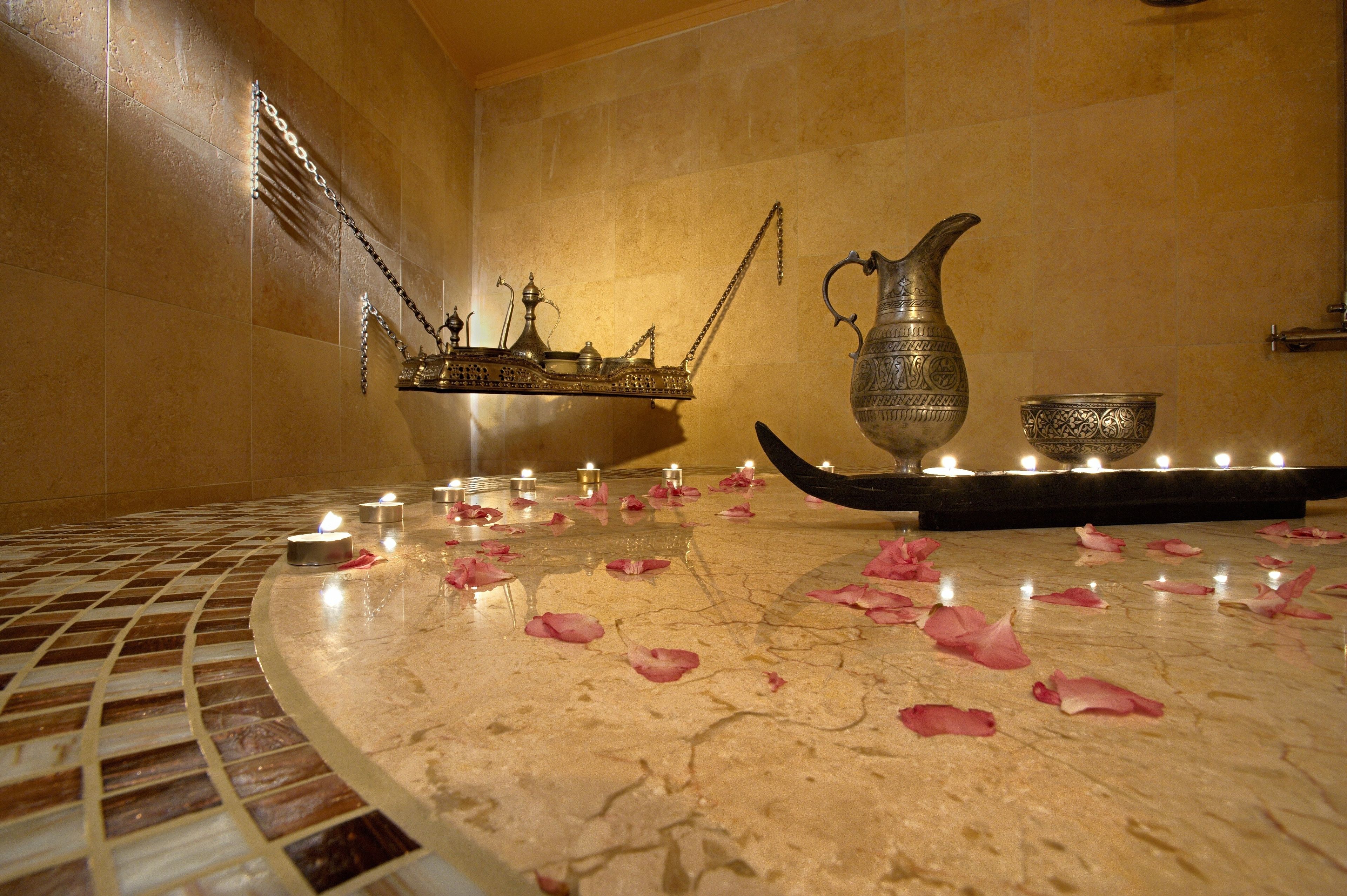A marble-tiled floor with rose petals and candles, a metal pitcher, and a small ornate table with a candle holder.