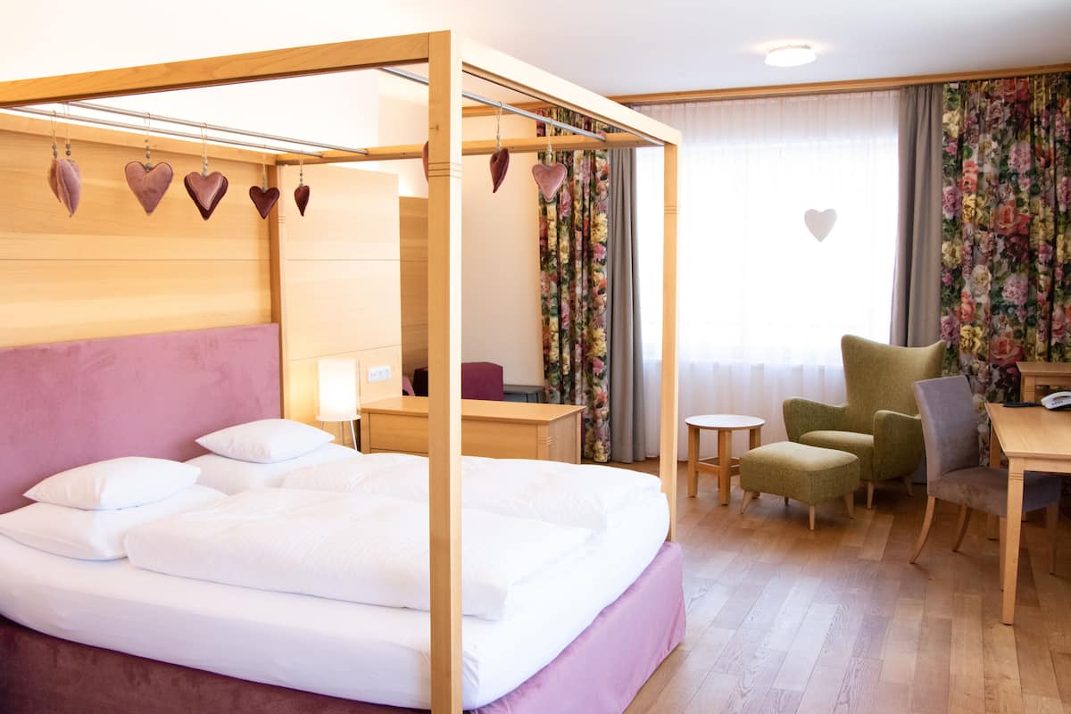 A bedroom with a four-poster bed, a desk, a chair, and a small table.