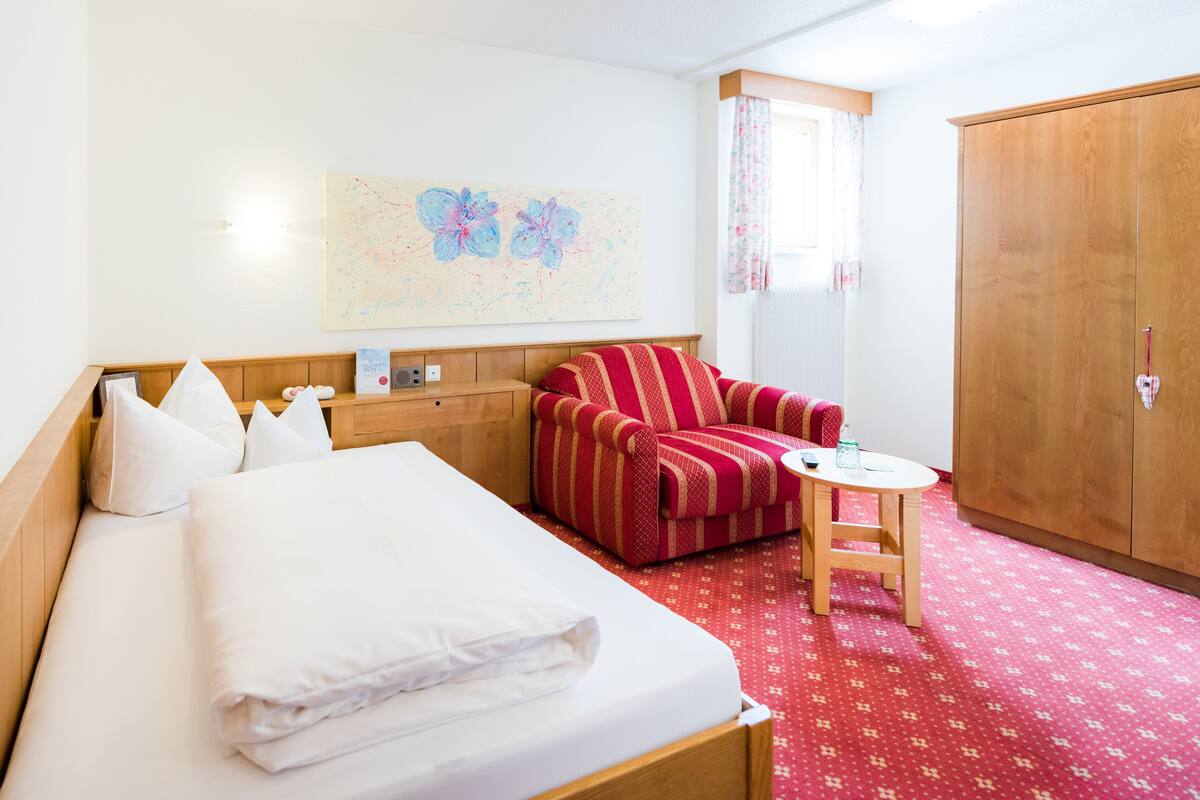 A hotel room with a bed, a red striped armchair, a small table, and a wardrobe.
