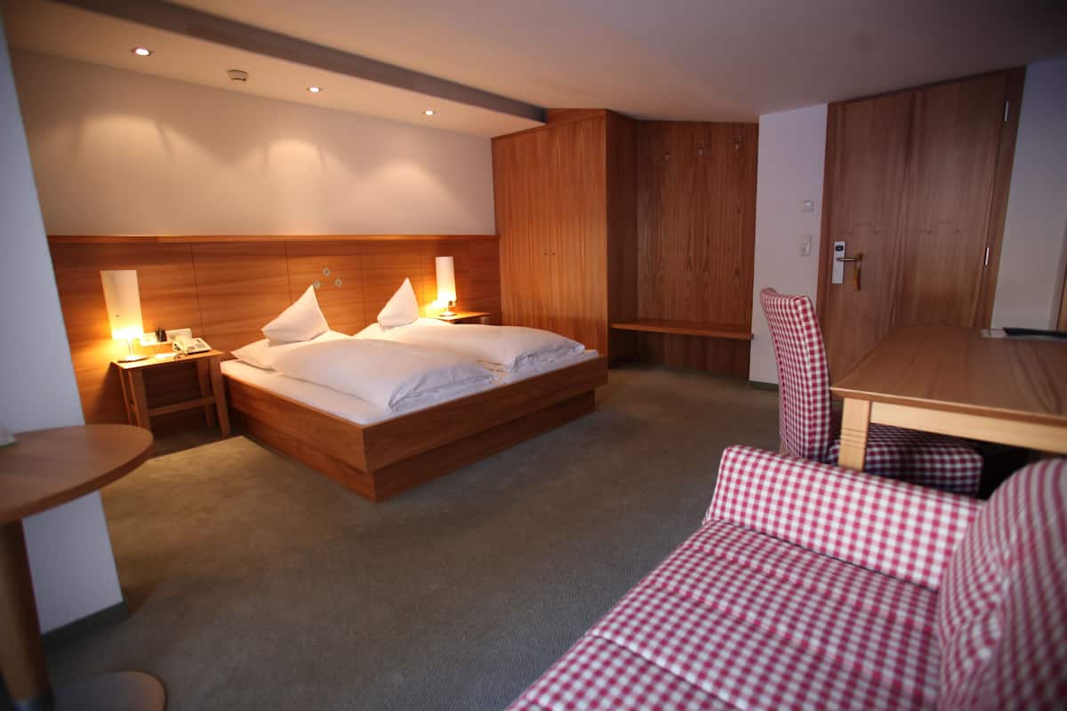 A hotel room with a wooden bed, bedside tables with lamps, a checkered chair, and a wooden wardrobe.