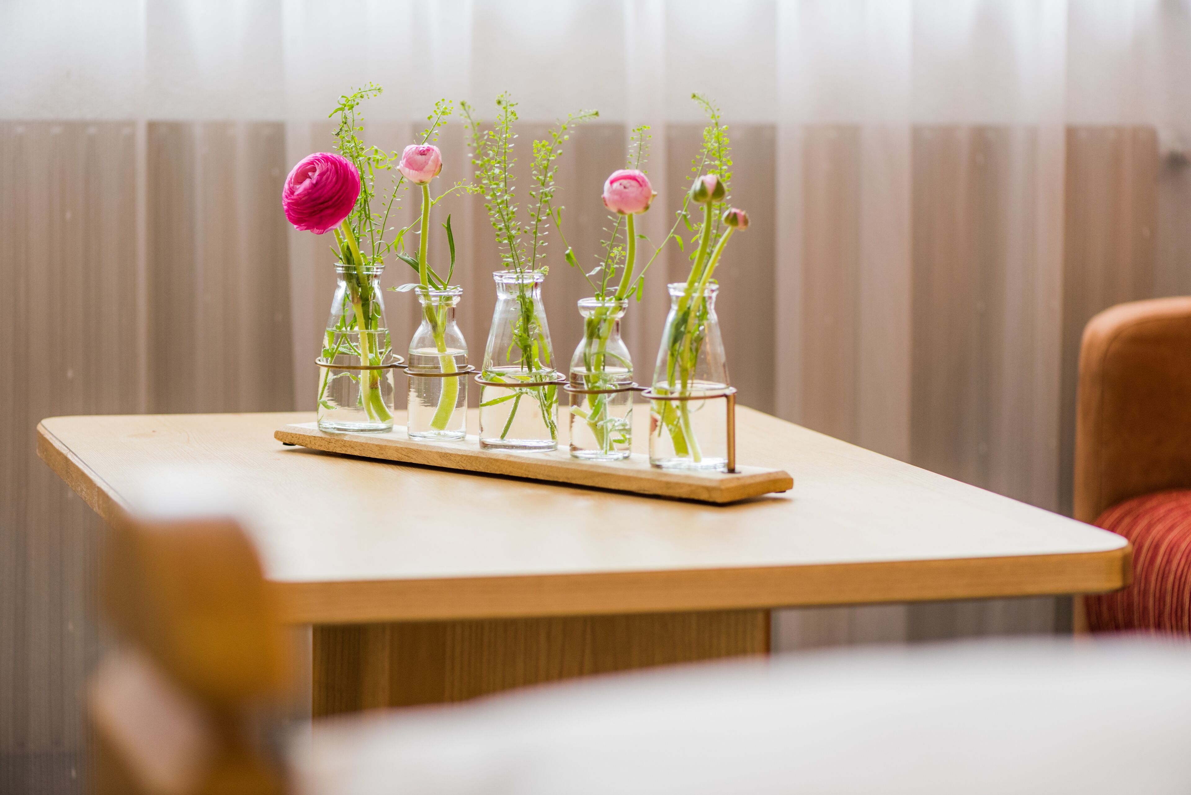 A table with five glass vases containing flowers and greenery, arranged in a row.